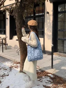 Dettaglio della borsa tote in maglia blu a cuori indossata da una modella all'aperto