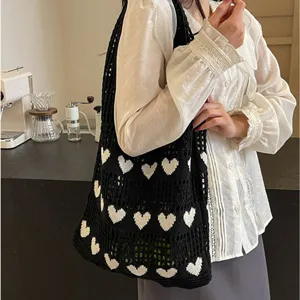 Detailed view of a stylish black knit tote bag with white heart patterns on a female model