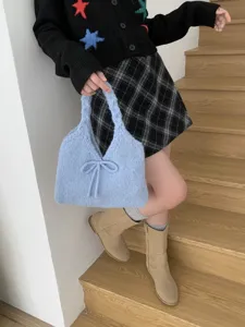 Light blue knitted handbag with bow detail being held by model on wooden stairs.