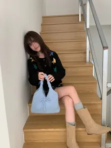 Lifestyle shot of a stylish light blue knitted handbag with a bow detail on stairs.