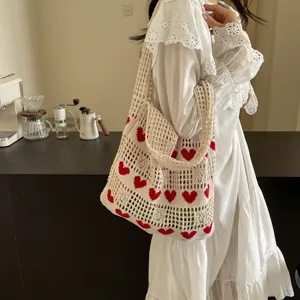 Woman wearing a white dress carrying a cream knitted tote bag with red heart patterns