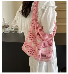 Detail of a pink heart knitted tote bag with hollow-out crochet design on a shoulder.