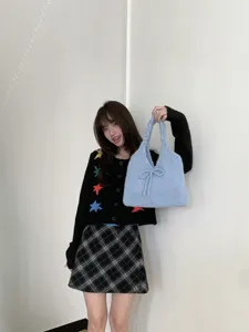 Model carrying a cute light blue knitted tote bag with a bow detail.