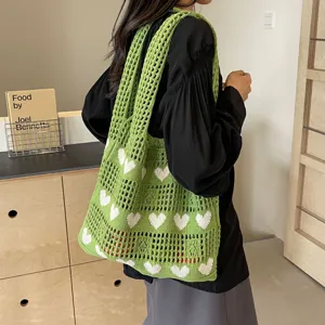 Green knitted hollow-out tote bag with white heart patterns shown on a model's shoulder