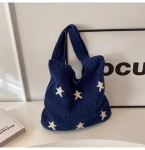 Close-up of a navy blue knitted tote bag featuring a white star pattern and cable knit design.