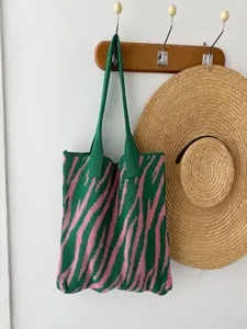 Stylish green and pink zebra pattern knitted tote bag hanging with a straw hat on a wall hook