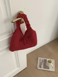 Detail of a red knitted winter underarm bag with a bow accent hanging on a white door