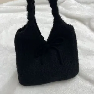 Close-up detail of a black knitted handbag with a delicate bow on a soft white background