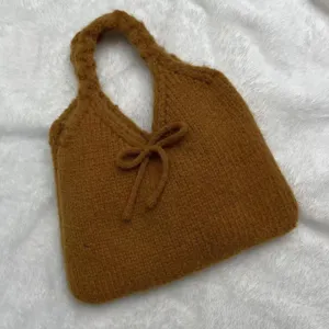 Detailed macro view of a cozy brown knitted underarm handbag with a decorative bow.