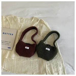 Two mini knitted handbags in brown and dark green colors displayed on a cream fabric