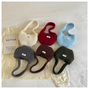 Collection of six colorful knitted mini handbags with egg labels on a cream blouse.