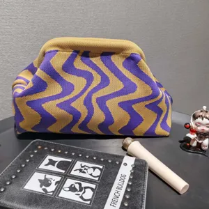 Detail view of a knitted wavy pattern clutch bag with cosmetic accessories on a desk