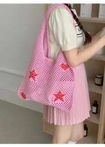 Detail view of pink hollow knit tote bag with red star motifs carried by model