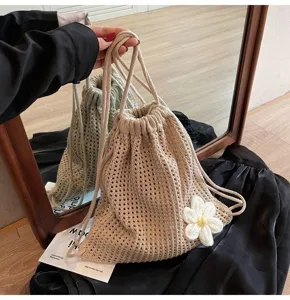 Detalle de mochila tejida beige con cordón y un adorno de flor blanca.