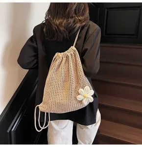 Vista trasera de una mochila de punto beige con accesorio de amuleto de flor blanca