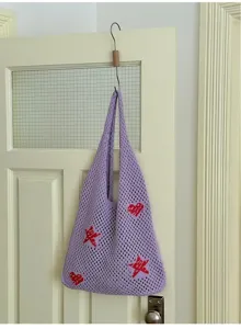 Purple knit hollow tote bag with red heart and star patterns hanging on a door hook.