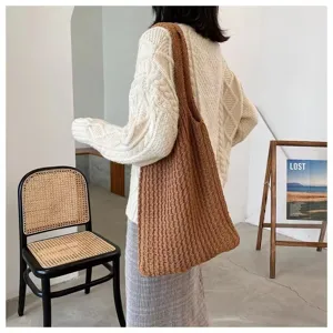 Large brown knitted tote bag worn over the shoulder in a minimalist indoor room