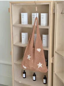 Close-up view of a brown hollow knitted tote bag featuring white star and heart patterns
