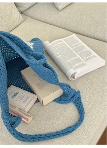 Lifestyle detail view of a blue crochet knit tote bag resting on a beige sofa