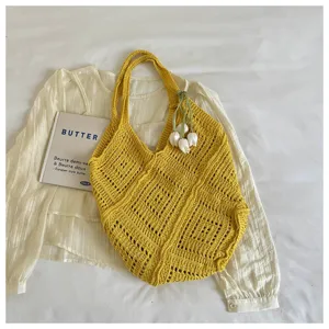 Close-up of a yellow crochet beach bag with intricate hollow-out patterns and a white floral charm.
