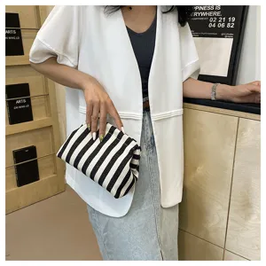 Détail d'une pochette nuage chic à rayures noires et blanches tenue à la main.