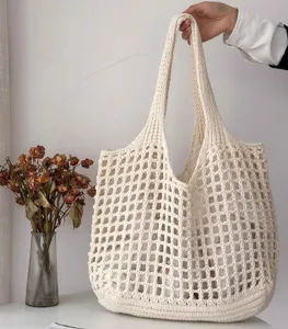 Vue tenue à la main d'un sac cabas en maille écrue avec un design au crochet minimaliste.