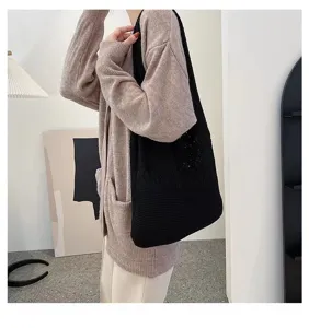Detail view of a large black hollow-out knitted tote bag worn by a model in a casual setting