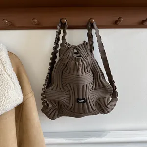 Casual dark brown knitted woven backpack with unique wavy straps hanging on a wall