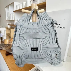 Close-up detail of a light grey pleated knit dual-use backpack on a wooden lifestyle stand