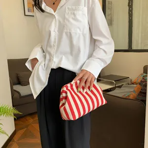 Pochette nuage chic à rayures rouges et blanches tenue par un mannequin dans un décor élégant.