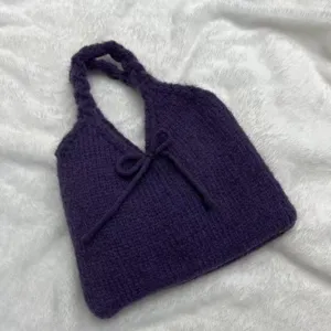 Hand-knitted deep purple shoulder bag featuring a cute bow detail on white faux fur surface.