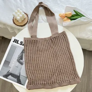 Detailed top view of brown knitted hollow tote bag on white table with lifestyle props