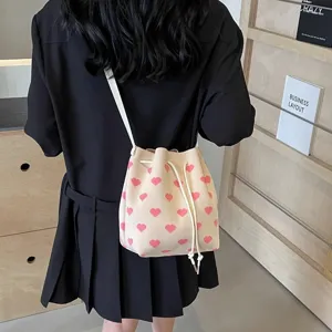 Cream white drawstring bucket bag with pink heart pattern and slim shoulder strap
