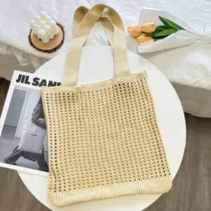 Detail view of a beige knitted hollow-out tote bag on a white table with floral props