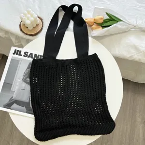 Detailed view of a black knitted hollow woven tote bag in a minimalist lifestyle setting