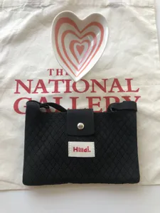 Detailed view of the black knitted crossbody bag with flap, snap closure and brand label.