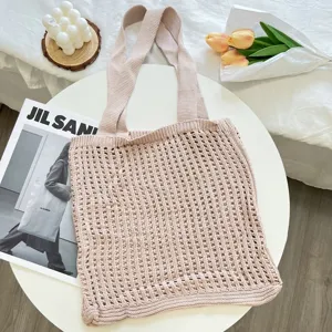 Detailed view of dusty pink knitted mesh tote bag on white table with lifestyle props