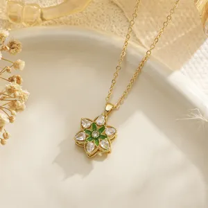 Close-up detail of a delicate gold flower pendant necklace with green and clear gemstones