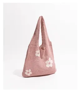 Vista detallada de un bolso de punto rosa con patrón floral blanco y malla calada