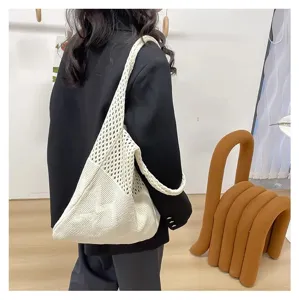 Vista detallada de un elegante bolso tote de punto calado beige sobre un blazer negro en estudio.