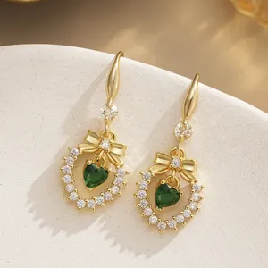 Detailed macro view of gold-plated bow earrings with emerald green heart zircons