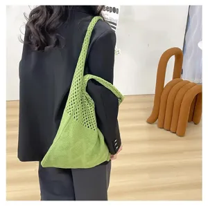 Vista detallada de un bolso tote de punto calado verde combinado con una chaqueta negra.