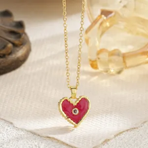 Macro shot of a gold necklace with a red enamel heart pendant and a sparkling central zircon