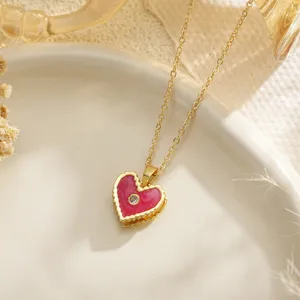 Macro detail of a gold chain necklace featuring a red enamel heart pendant with zircon stone