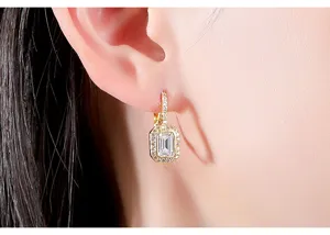 Close-up of gold plated huggie earring with emerald cut zircon stone on ear.