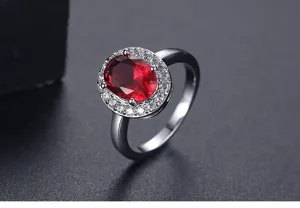 Primer plano de elegante anillo plateado con piedra preciosa roja ovalada y halo de circonita