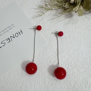 Elegant red bead tassel earrings with silver chain on textured white background