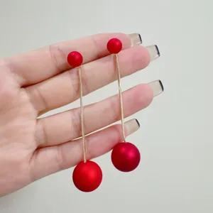 Elegant long red ball tassel earrings shown being held by a hand close up view