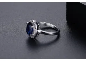 Detalle macro de un elegante anillo con gema azul óvalo y halo de circonitas brillantes.
