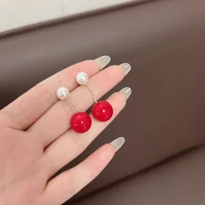Close-up detail of elegant gold tassel earrings with white pearls and red beads